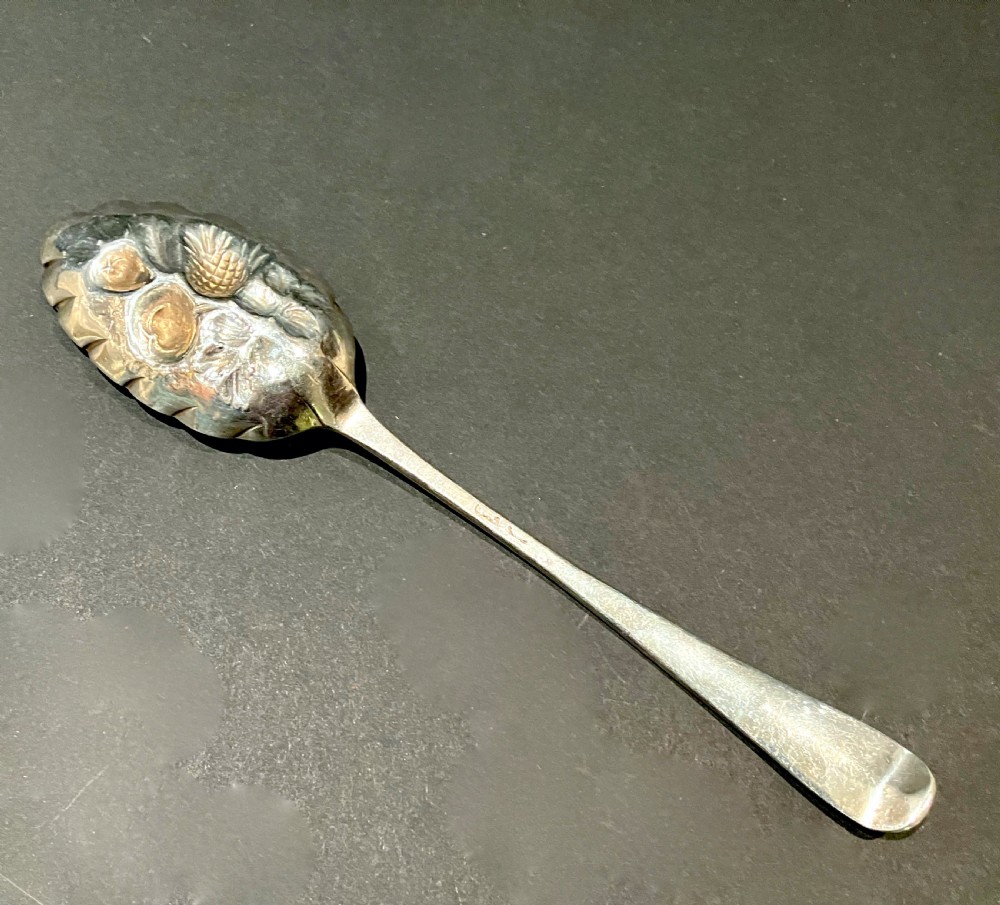 A George III silver berry spoon featuring embossed fruit detail inside the bowl and an intricately engraved handle. View II