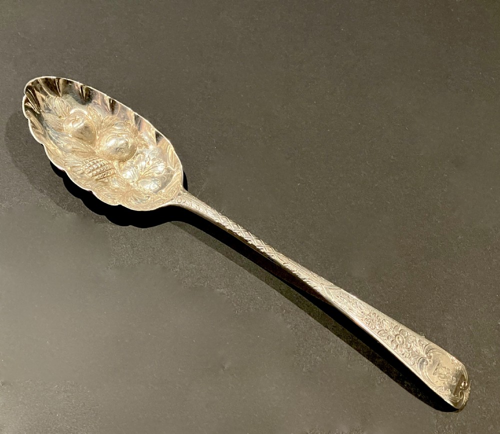A George III silver berry spoon featuring embossed fruit detail inside the bowl and an intricately engraved handle.