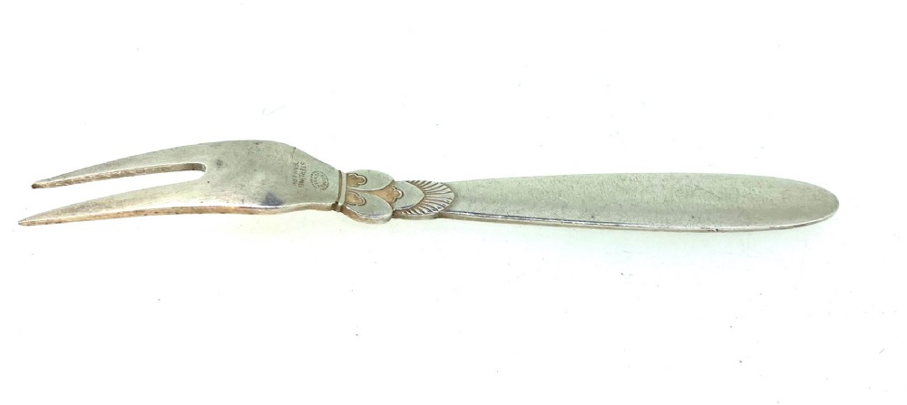 A Georg Jensen sterling silver two-prong serving fork featuring detailed decorative carving at the neck and a smooth tapered handle.