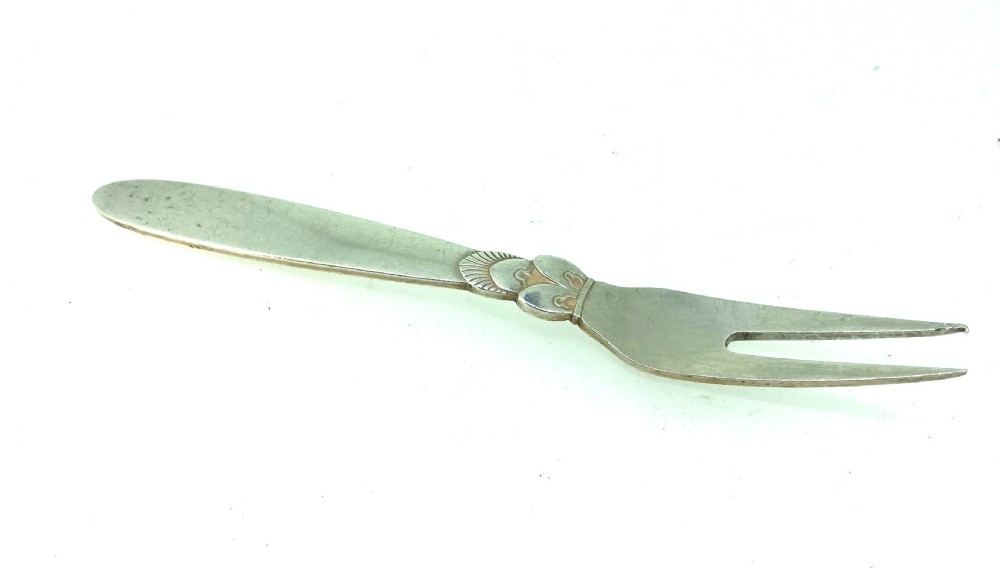 A Georg Jensen sterling silver two-prong serving fork featuring detailed decorative carving at the neck and a smooth tapered handle. View II