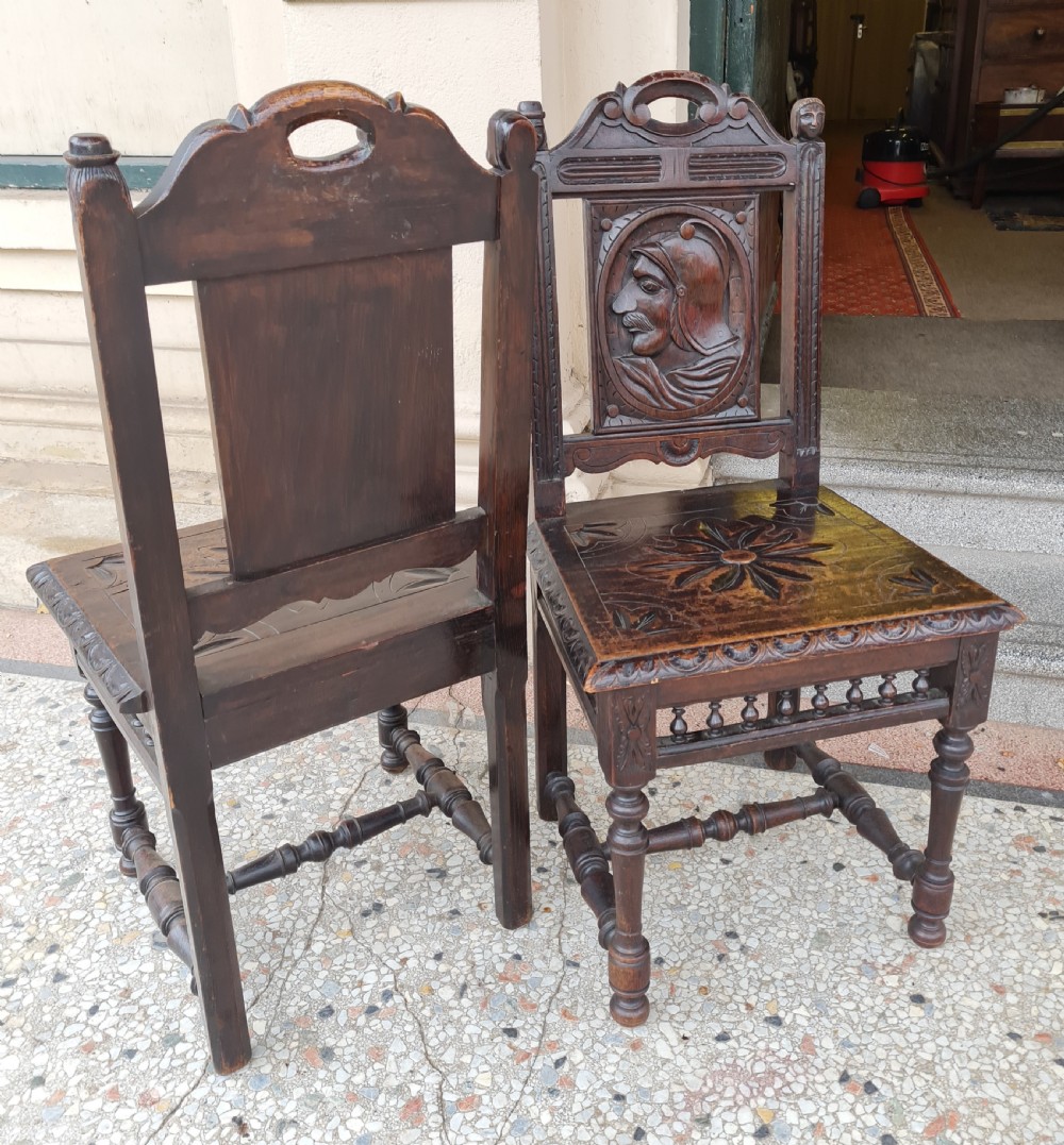 A pair of dark carved oak hall chairs featuring carved portrait medallions on the backrests and starburst carvings on the timber seats. View IV