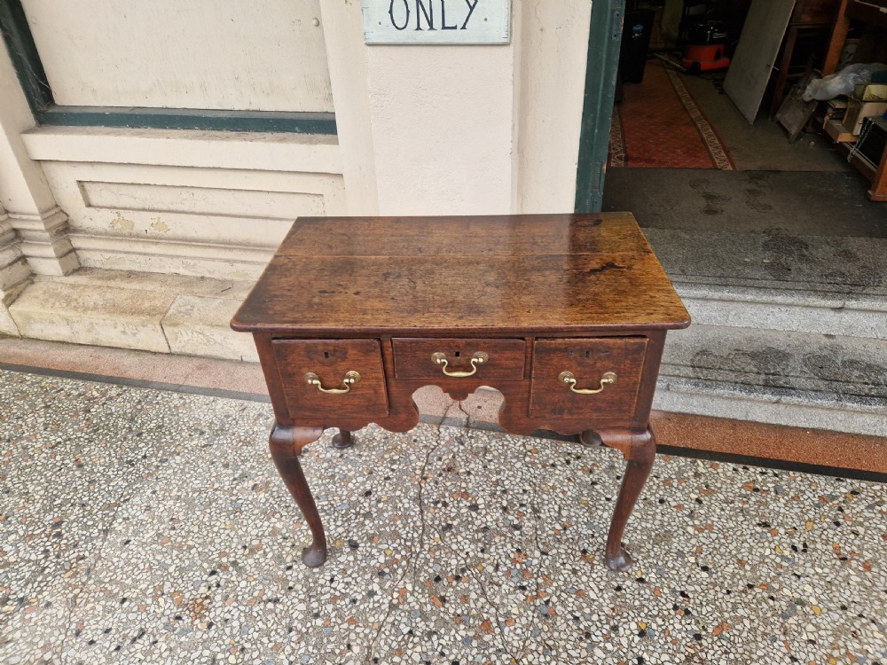 An antique oak lowboy featuring three drawers with brass drop handles, a scalloped apron, and four cabriole legs resting on pad feet. View VI