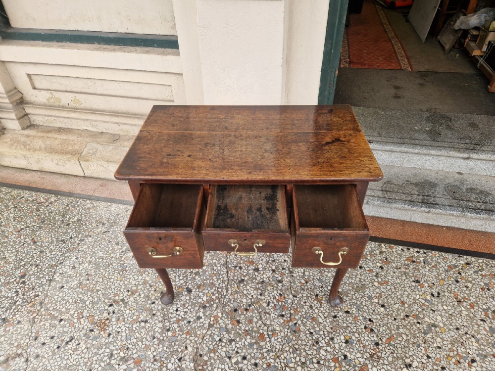 An antique oak lowboy featuring three drawers with brass drop handles, a scalloped apron, and four cabriole legs resting on pad feet. View VIII