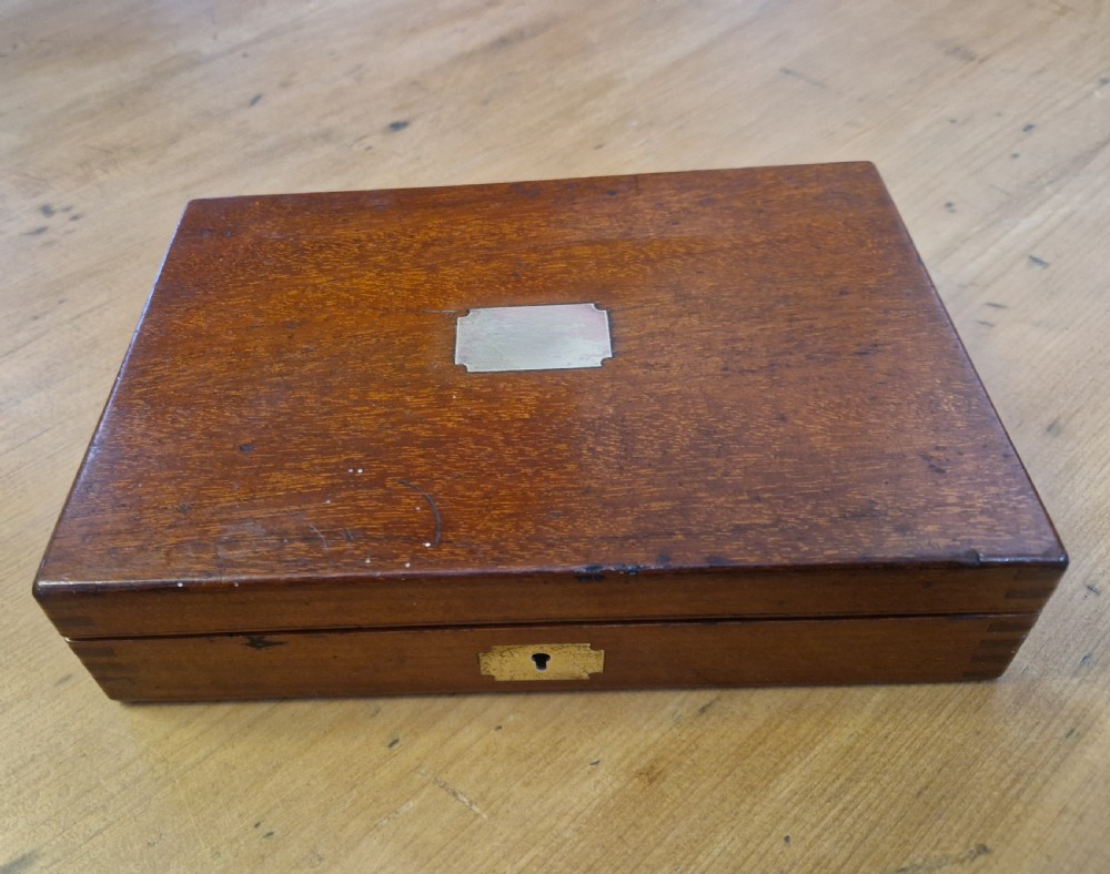 A closed rectangular Edwardian mahogany box featuring a brass keyhole escutcheon on the front and a blank metal cartouche inlaid into the top lid.