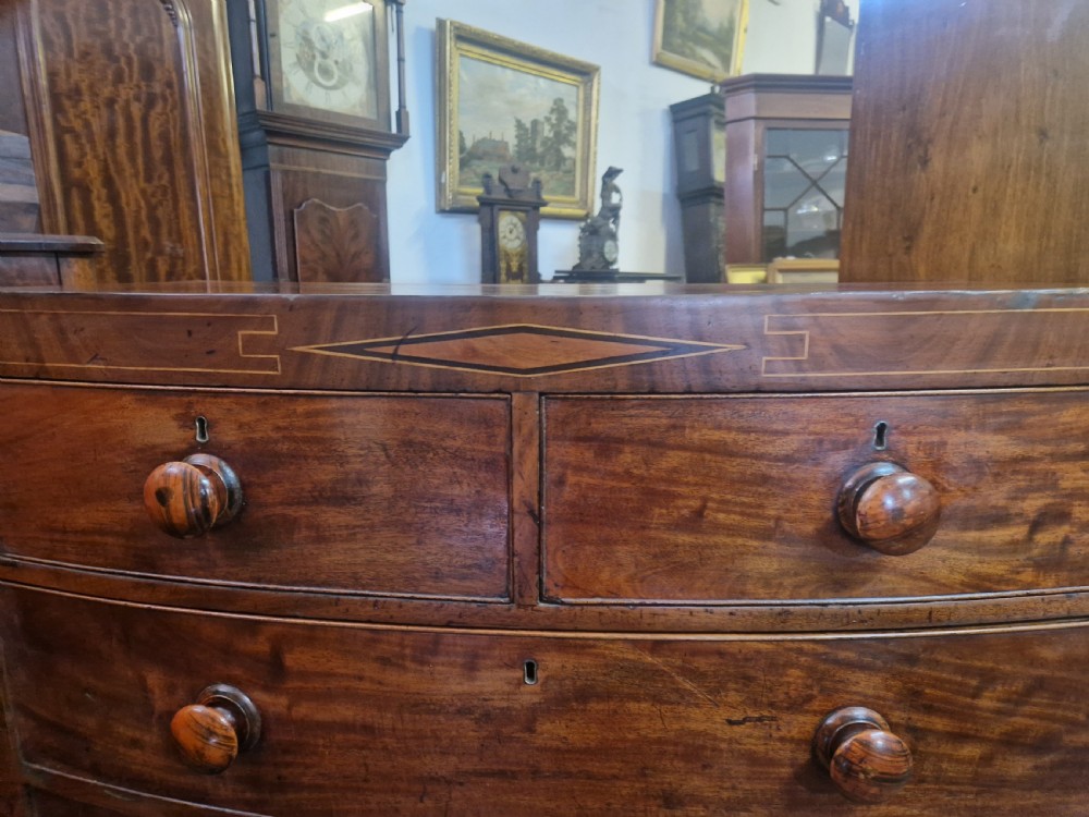 A Georgian mahogany bow front chest of drawers featuring two short over three long graduated drawers with turned wooden knobs and delicate geometric inlay. View IV