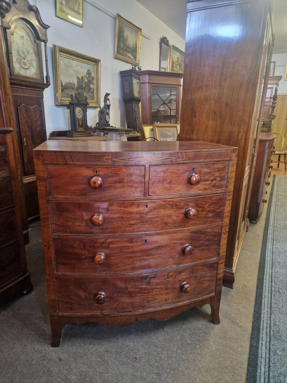 A Georgian mahogany bow front chest of drawers featuring two short over three long graduated drawers with turned wooden knobs and delicate geometric inlay.