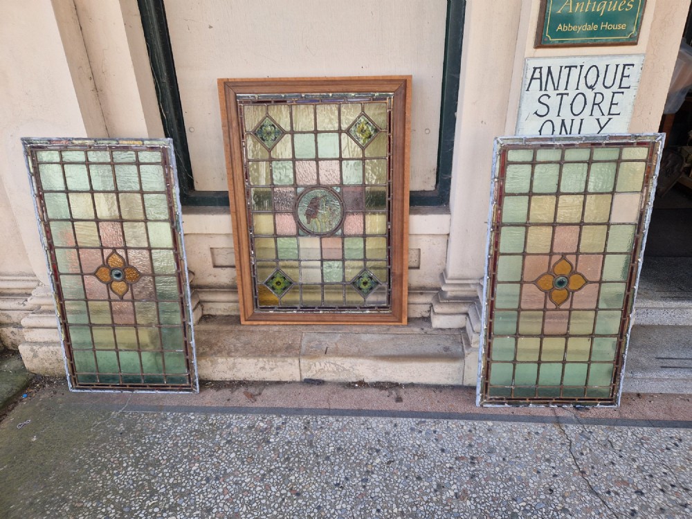 A rectangular Victorian leaded glass panel set in a timber frame, featuring pastel geometric panes, four decorative corner inserts, and a central roundel depicting a hand-painted bird. View III