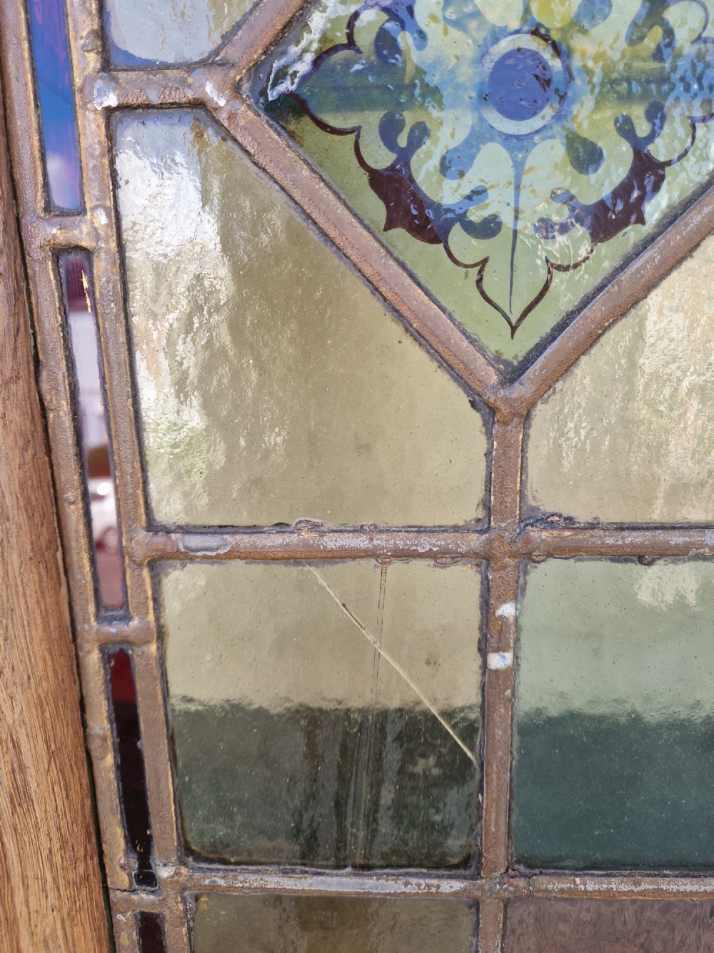 A rectangular Victorian leaded glass panel set in a timber frame, featuring pastel geometric panes, four decorative corner inserts, and a central roundel depicting a hand-painted bird. View V