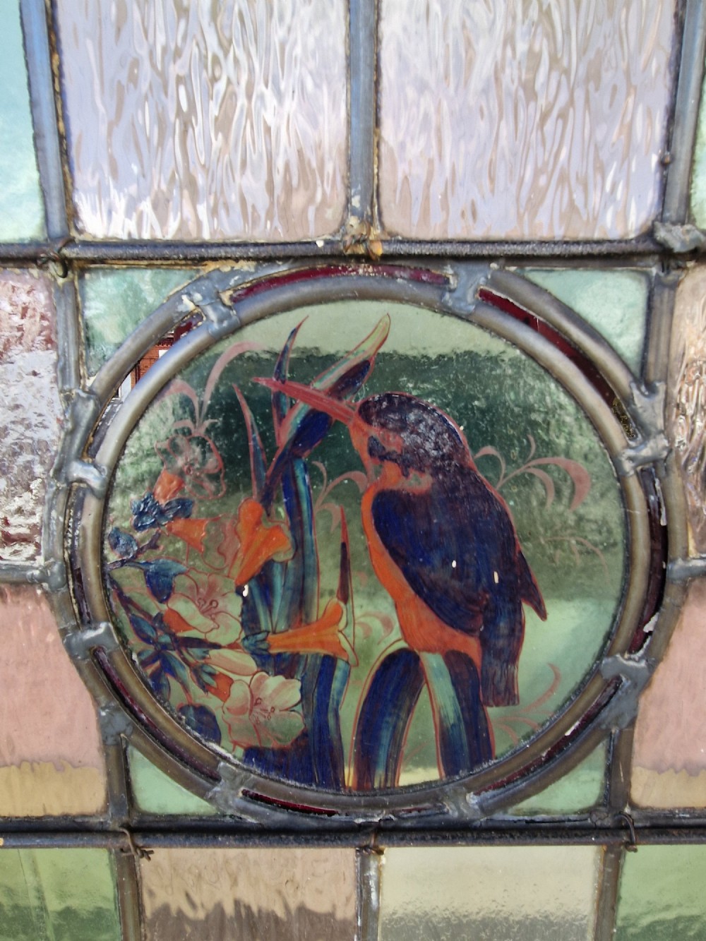 A rectangular Victorian leaded glass panel set in a timber frame, featuring pastel geometric panes, four decorative corner inserts, and a central roundel depicting a hand-painted bird. View VI