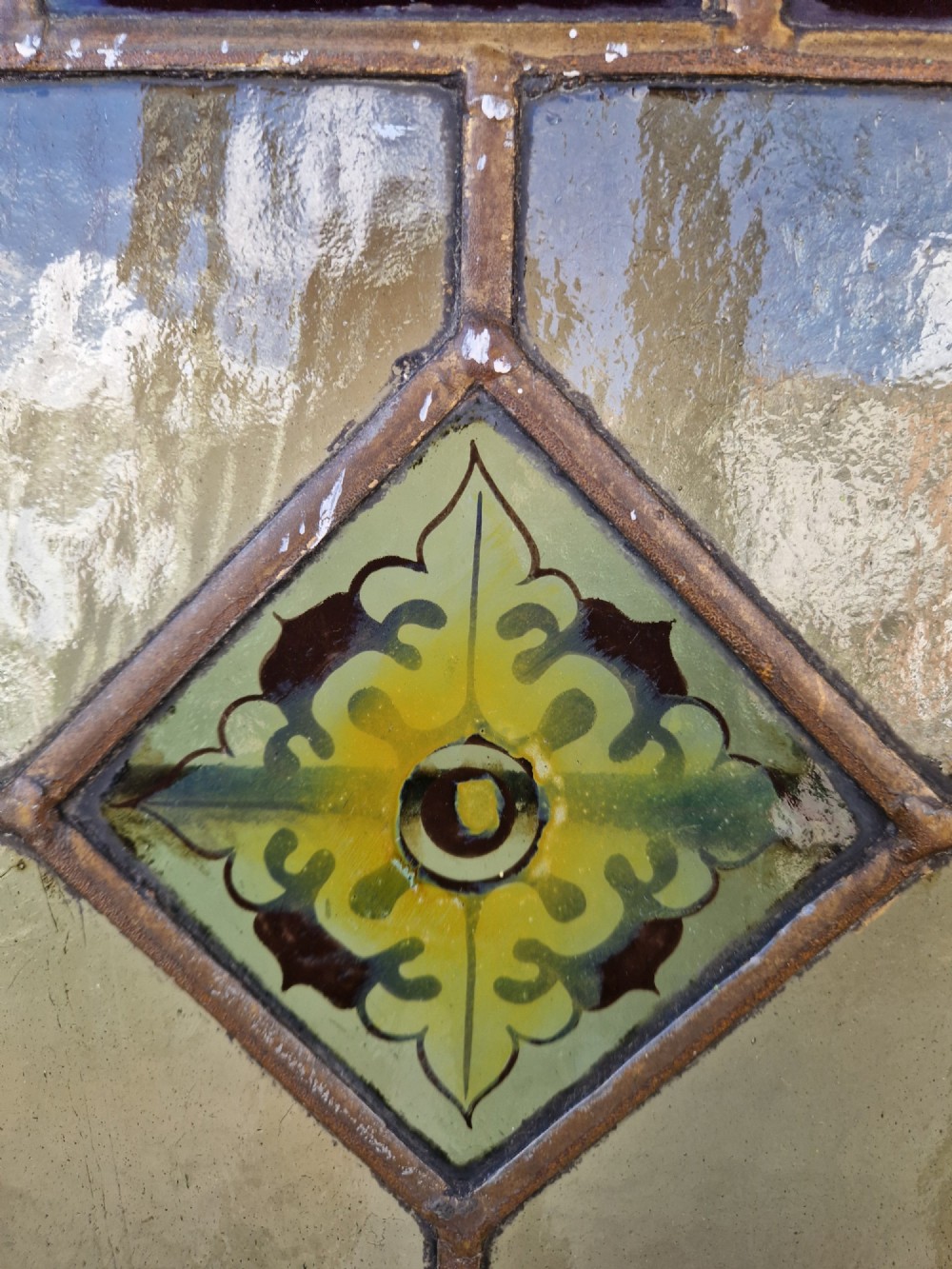 A rectangular Victorian leaded glass panel set in a timber frame, featuring pastel geometric panes, four decorative corner inserts, and a central roundel depicting a hand-painted bird. View IX