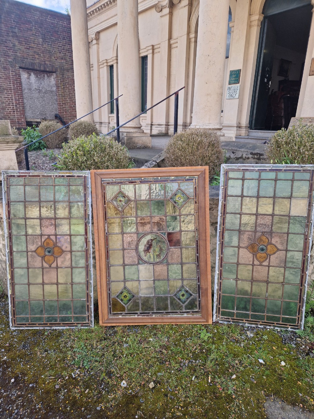 A rectangular Victorian leaded glass panel set in a timber frame, featuring pastel geometric panes, four decorative corner inserts, and a central roundel depicting a hand-painted bird. View II