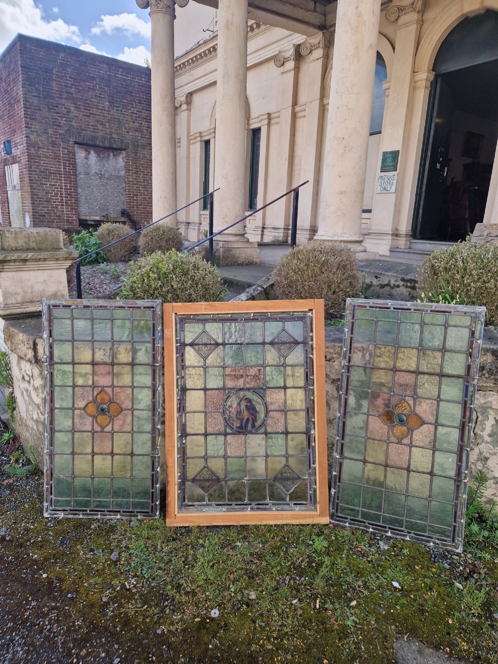 A rectangular Victorian leaded glass panel set in a timber frame, featuring pastel geometric panes, four decorative corner inserts, and a central roundel depicting a hand-painted bird. View XI