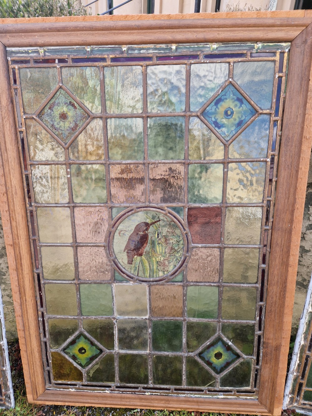 A rectangular Victorian leaded glass panel set in a timber frame, featuring pastel geometric panes, four decorative corner inserts, and a central roundel depicting a hand-painted bird. View XIII