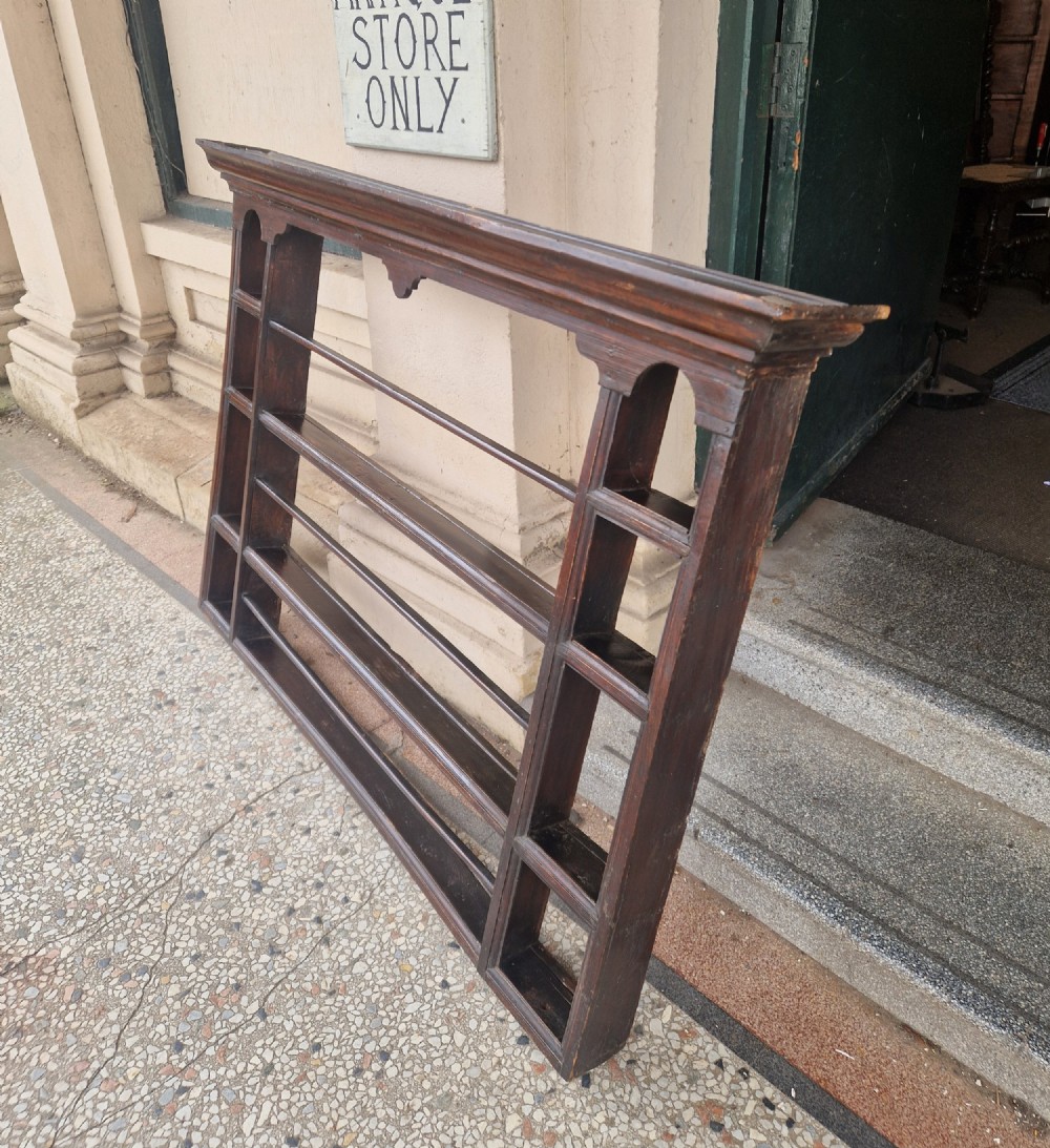 A dark-stained antique oak delft wall rack featuring open shelves, side compartments, and a heavy moulded cornice.