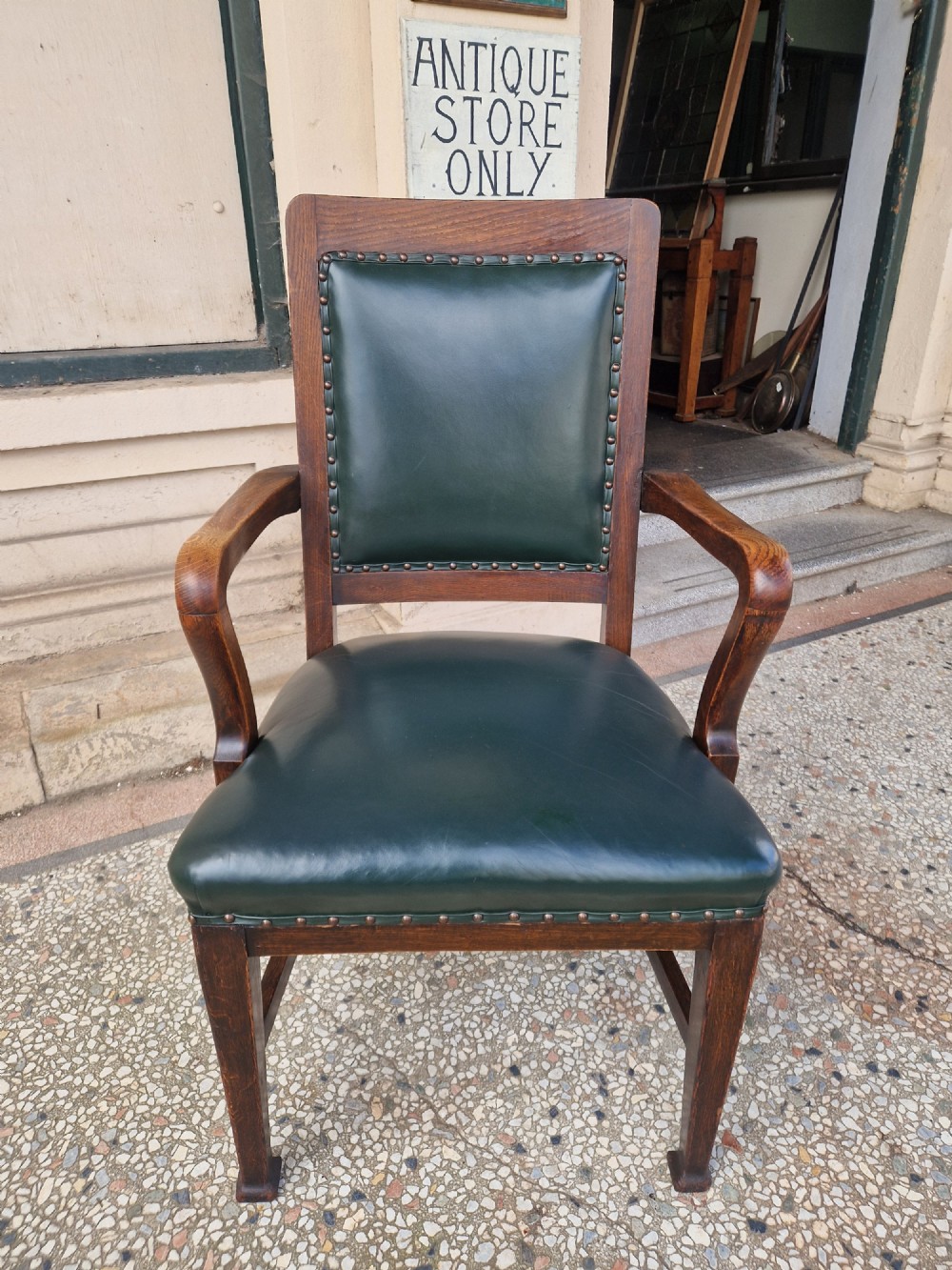 An antique Arts and Crafts oak armchair featuring dark green leather upholstery secured with decorative metal studs.