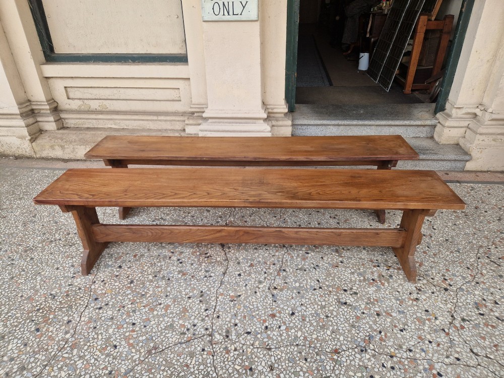 A pair of long solid oak benches featuring flat plank tops, trestle legs, and horizontal wooden stretchers.