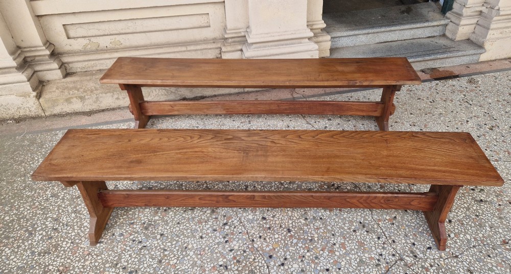A pair of long solid oak benches featuring flat plank tops, trestle legs, and horizontal wooden stretchers. View II