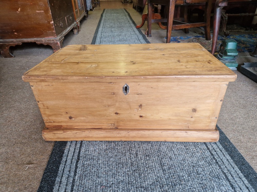 A rectangular antique pine storage box with a hinged lid, tapered sides, a moulded base, and an iron keyhole escutcheon on the front.