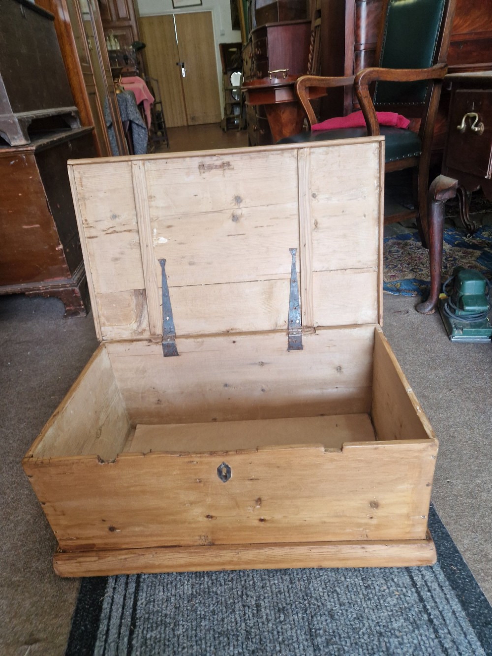 A rectangular antique pine storage box with a hinged lid, tapered sides, a moulded base, and an iron keyhole escutcheon on the front. View III