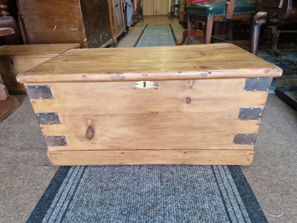 An antique pine blanket box featuring iron corner straps, a brass keyhole escutcheon, and a hinged lid.