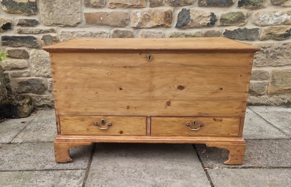 An antique Georgian pine mule chest featuring a lift-top lid, two lower drawers with brass drop handles, visible corner dovetail joints, and bracket feet.