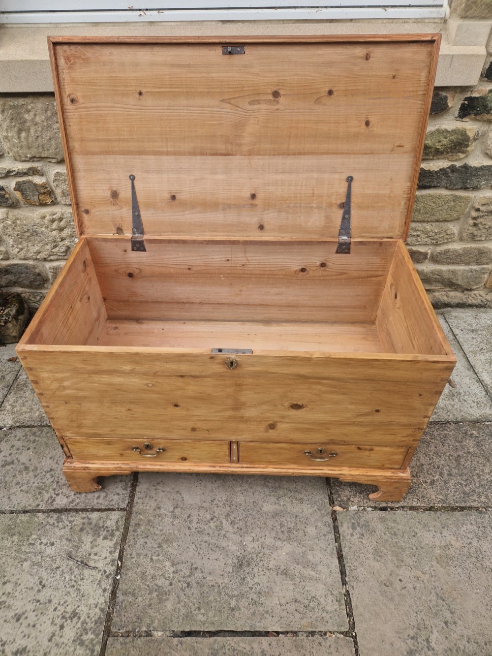 An antique Georgian pine mule chest featuring a lift-top lid, two lower drawers with brass drop handles, visible corner dovetail joints, and bracket feet. View V