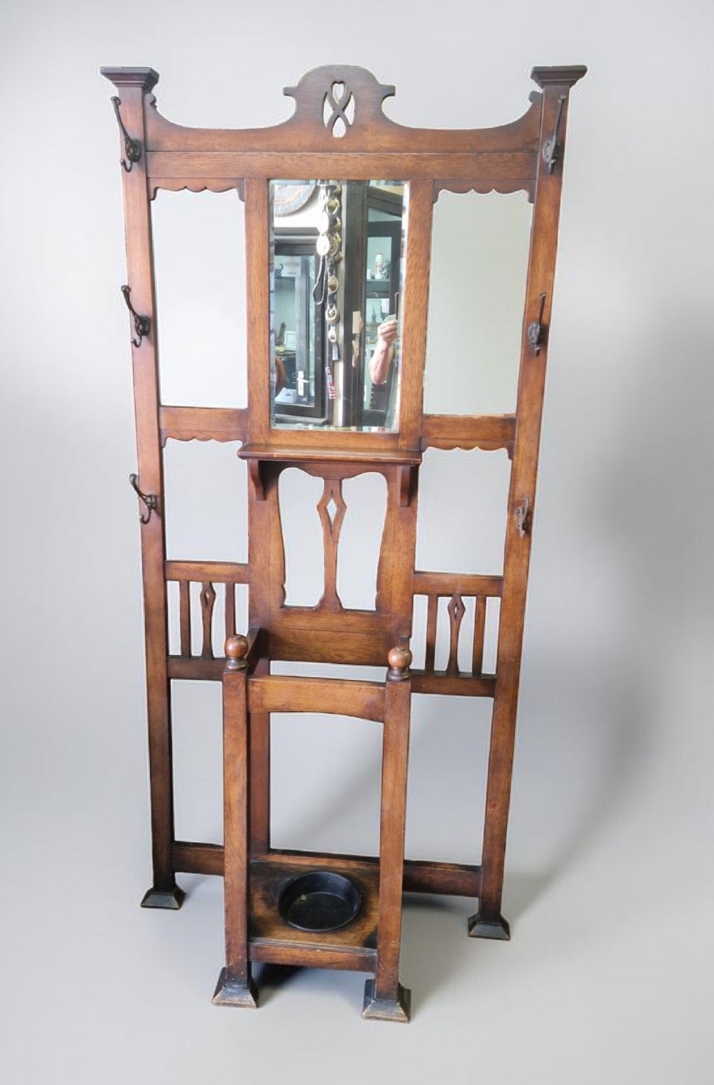 An Art Nouveau oak hall stand featuring a central rectangular mirror, coat hooks, stylized pierced motifs, and an integrated lower umbrella stand with a removable drip tray.