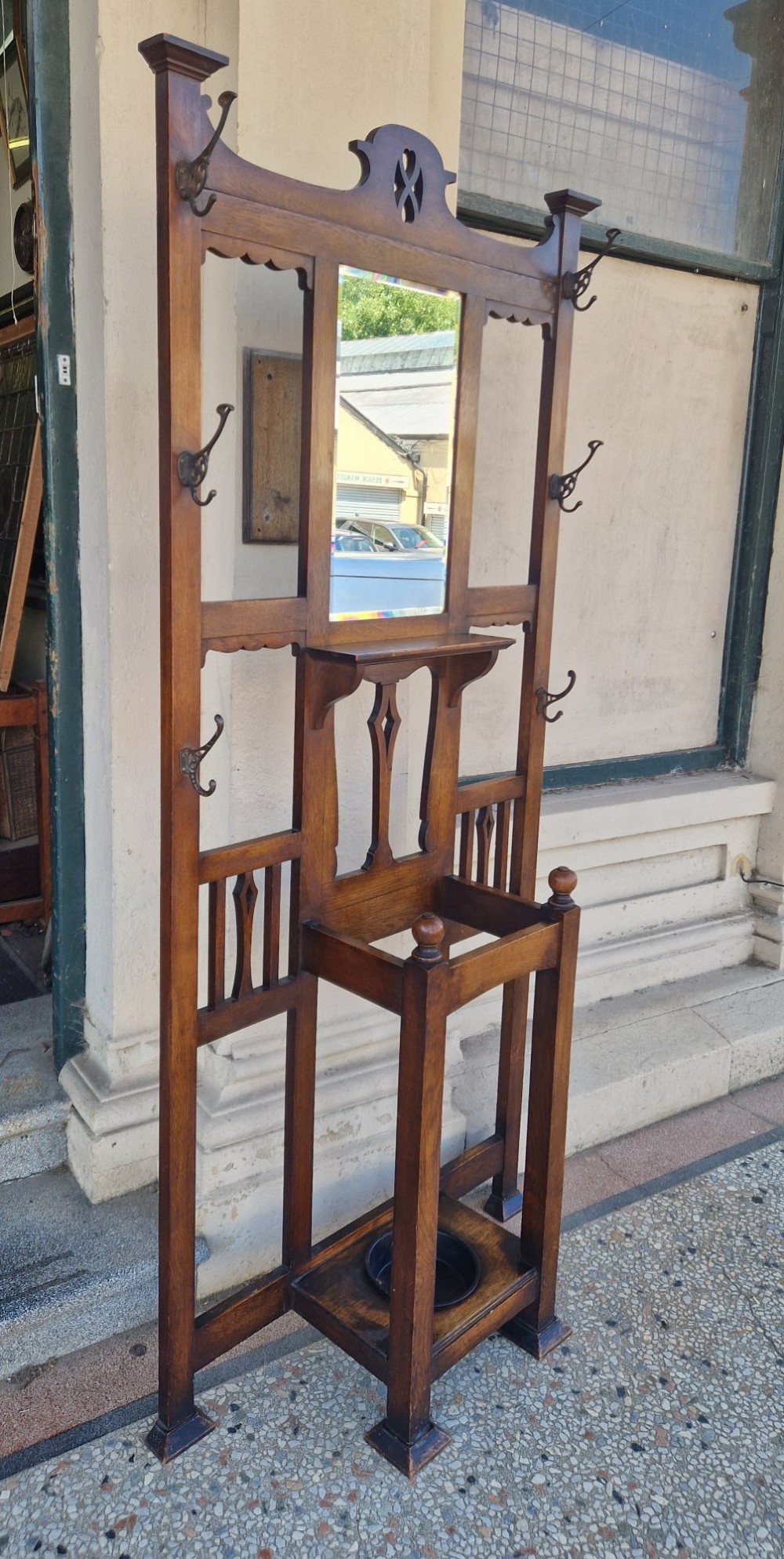 An Art Nouveau oak hall stand featuring a central rectangular mirror, coat hooks, stylized pierced motifs, and an integrated lower umbrella stand with a removable drip tray. View II