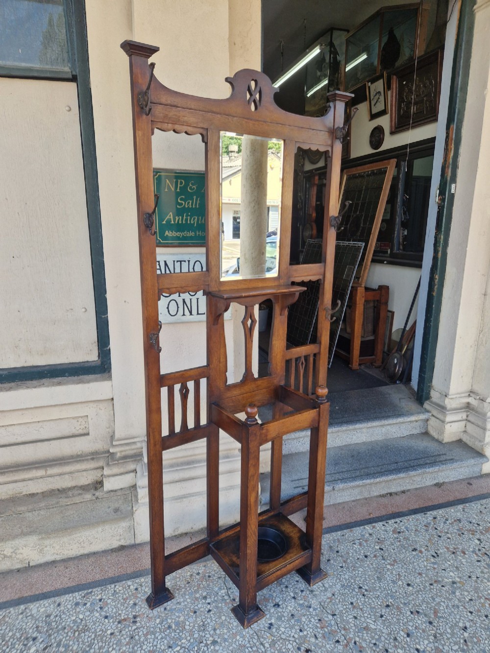 An Art Nouveau oak hall stand featuring a central rectangular mirror, coat hooks, stylized pierced motifs, and an integrated lower umbrella stand with a removable drip tray. View III