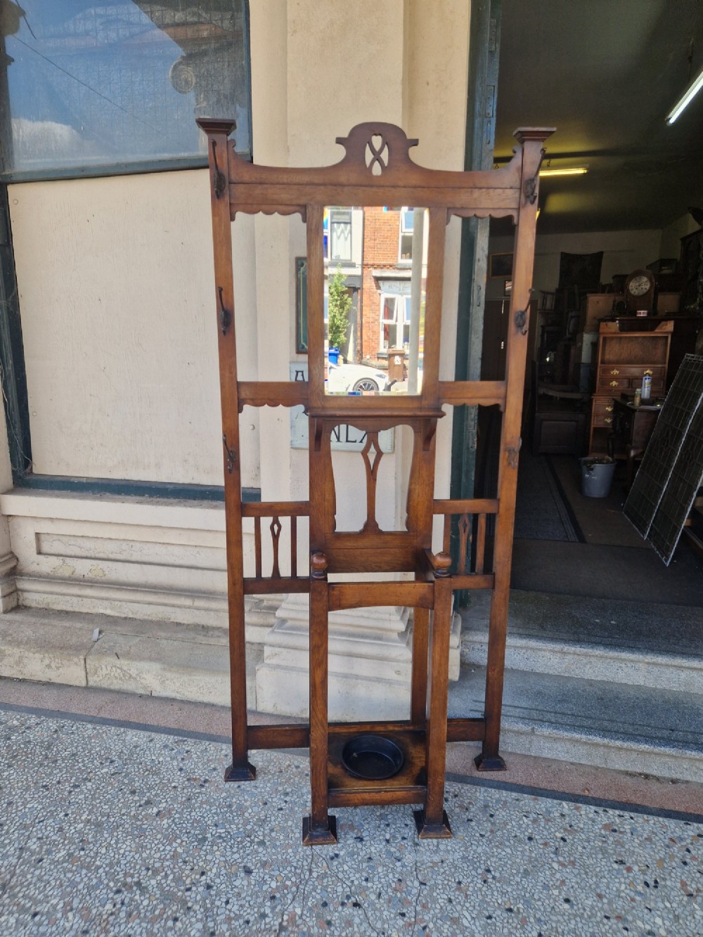 An Art Nouveau oak hall stand featuring a central rectangular mirror, coat hooks, stylized pierced motifs, and an integrated lower umbrella stand with a removable drip tray. View IV
