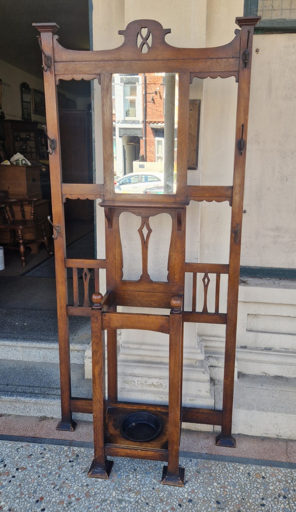 An Art Nouveau oak hall stand featuring a central rectangular mirror, coat hooks, stylized pierced motifs, and an integrated lower umbrella stand with a removable drip tray. View V