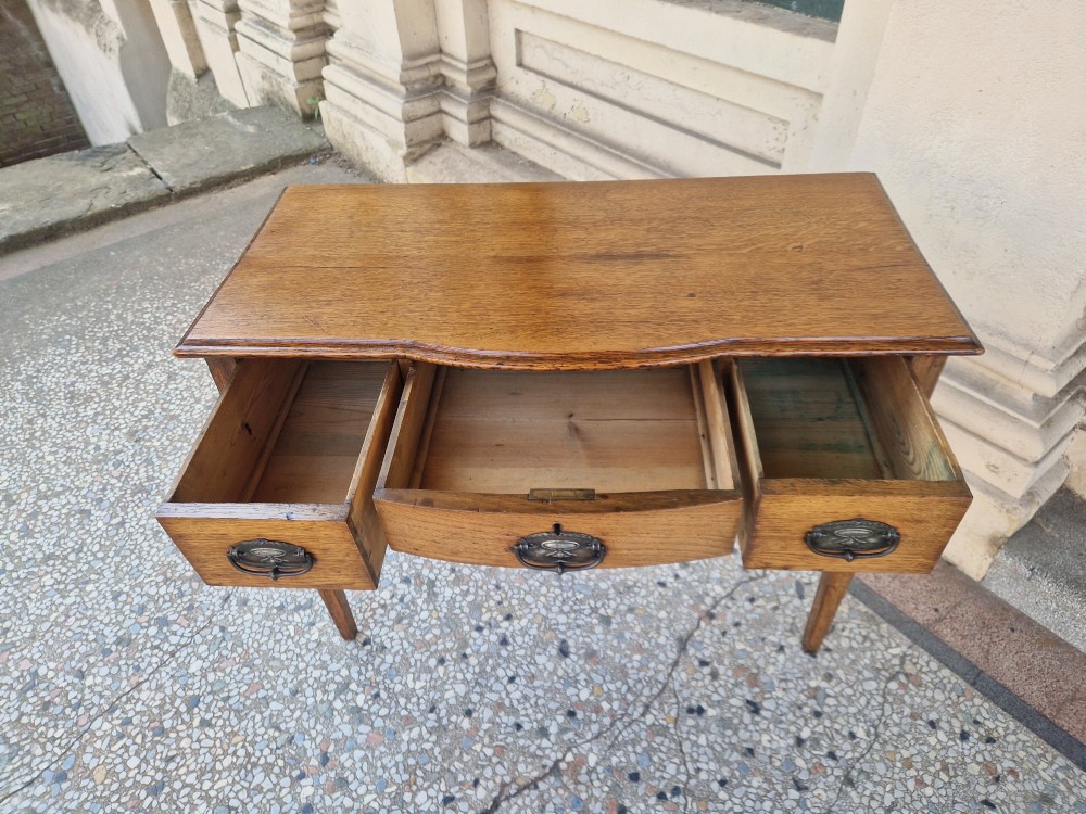 An Edwardian solid oak writing desk featuring three frieze drawers with metal drop handles, set on four square tapered legs against a neutral background. View III