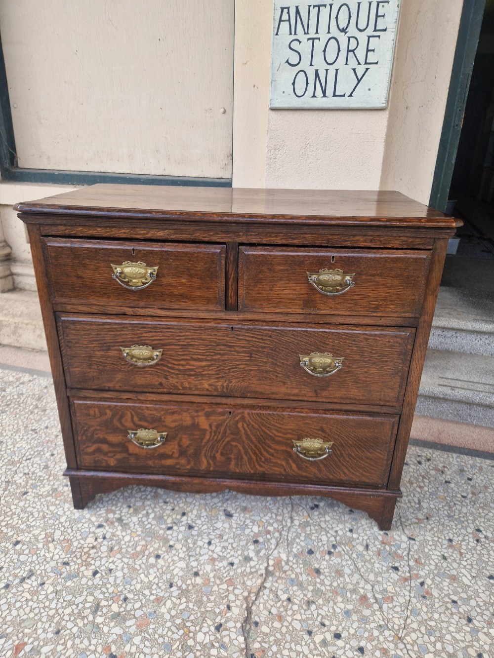An Edwardian solid oak chest of drawers with two short over two long drawers fitted with decorative brass handles. View II