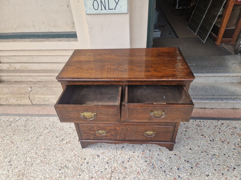 An Edwardian solid oak chest of drawers with two short over two long drawers fitted with decorative brass handles. View V
