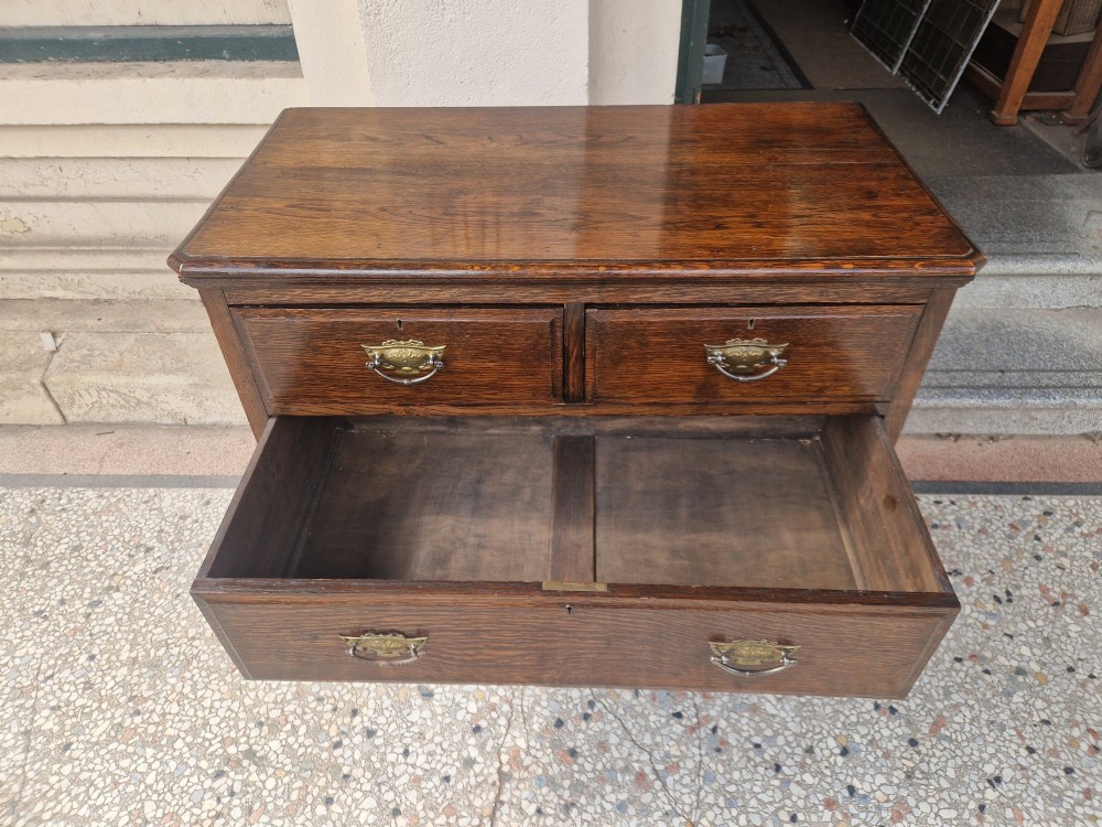 An Edwardian solid oak chest of drawers with two short over two long drawers fitted with decorative brass handles. View VI