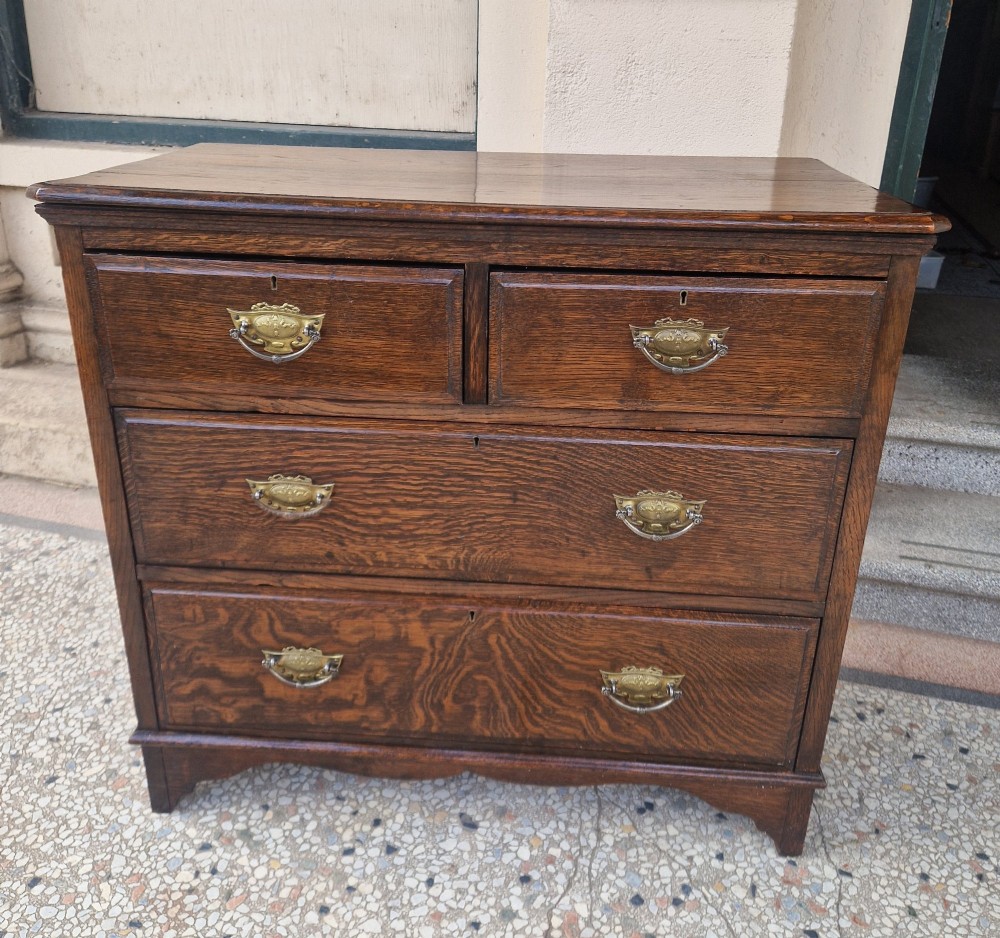 An Edwardian solid oak chest of drawers with two short over two long drawers fitted with decorative brass handles.