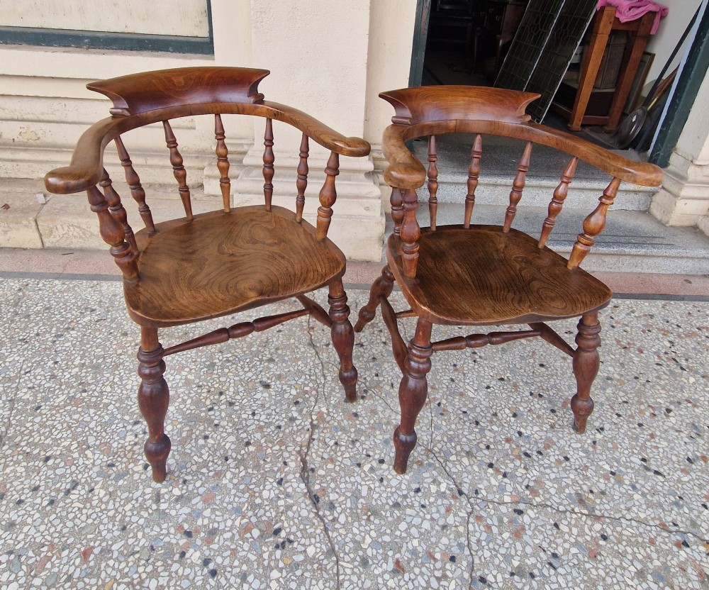 A pair of antique warm brown ash and elm captains armchairs featuring curved horseshoe backrests, turned spindles, shaped saddle seats, and turned legs. View IV