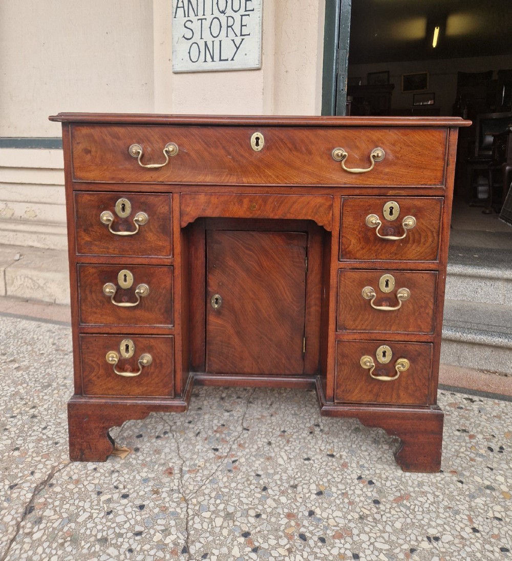 An 18th-century Georgian mahogany kneehole desk featuring a long top drawer, six flank drawers, a central recessed cupboard, brass drop handles, and bracket feet.