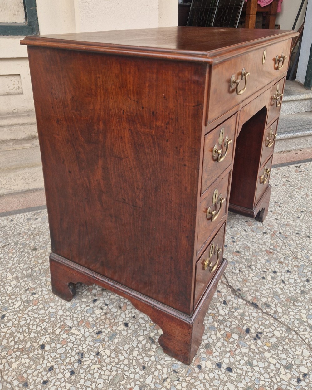 An 18th-century Georgian mahogany kneehole desk featuring a long top drawer, six flank drawers, a central recessed cupboard, brass drop handles, and bracket feet. View II