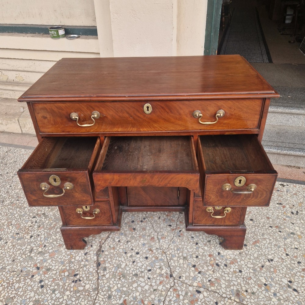 An 18th-century Georgian mahogany kneehole desk featuring a long top drawer, six flank drawers, a central recessed cupboard, brass drop handles, and bracket feet. View V