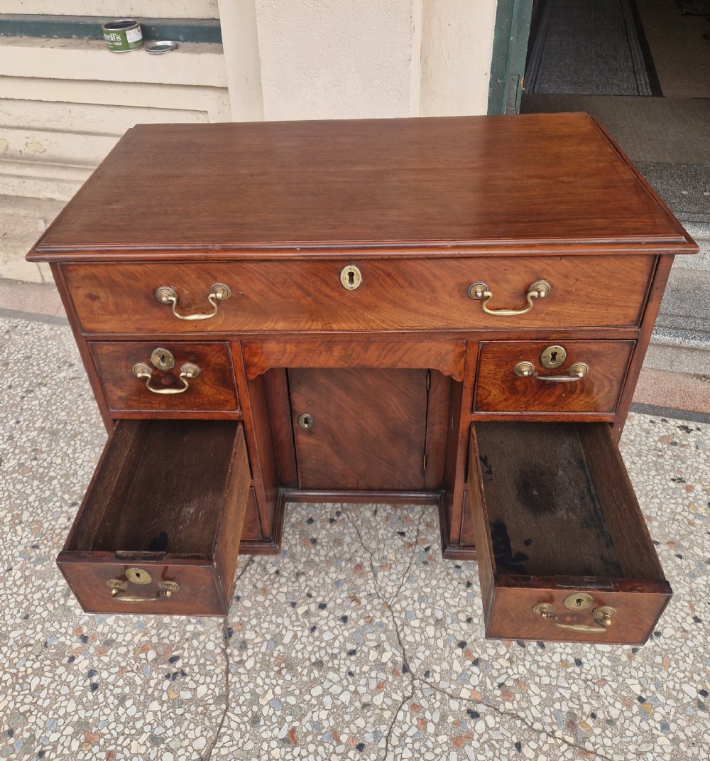 An 18th-century Georgian mahogany kneehole desk featuring a long top drawer, six flank drawers, a central recessed cupboard, brass drop handles, and bracket feet. View VI