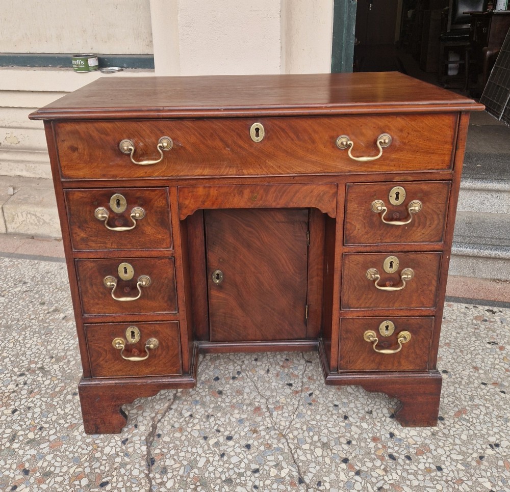 An 18th-century Georgian mahogany kneehole desk featuring a long top drawer, six flank drawers, a central recessed cupboard, brass drop handles, and bracket feet. View VIII