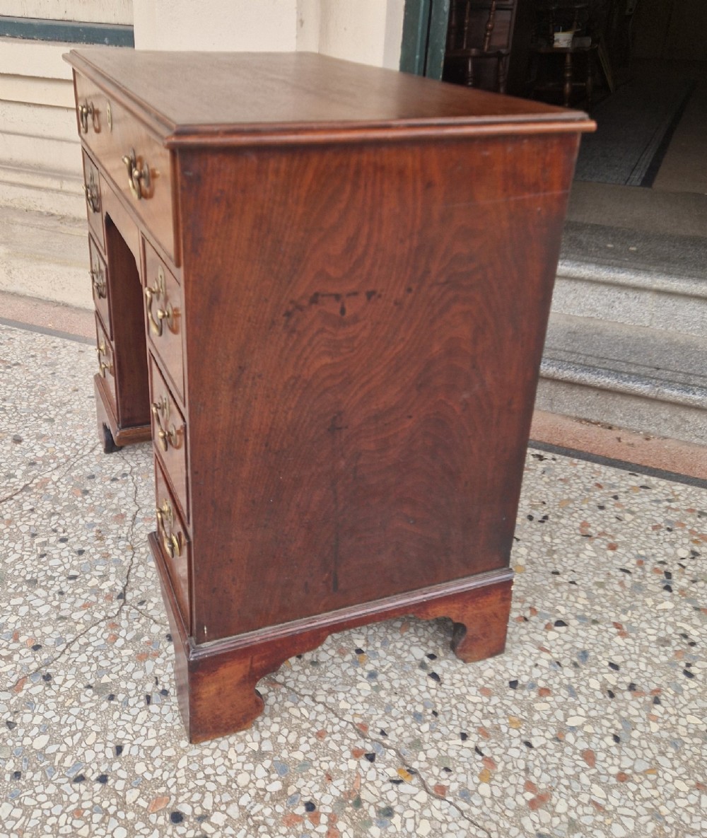 An 18th-century Georgian mahogany kneehole desk featuring a long top drawer, six flank drawers, a central recessed cupboard, brass drop handles, and bracket feet. View X