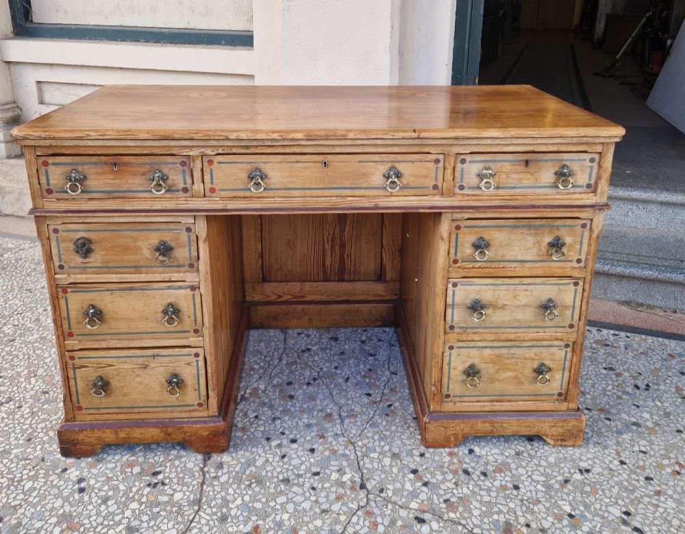 An Arts and Crafts pitch pine pedestal desk featuring nine drawers with hand-painted line borders and metal ring handles. View II