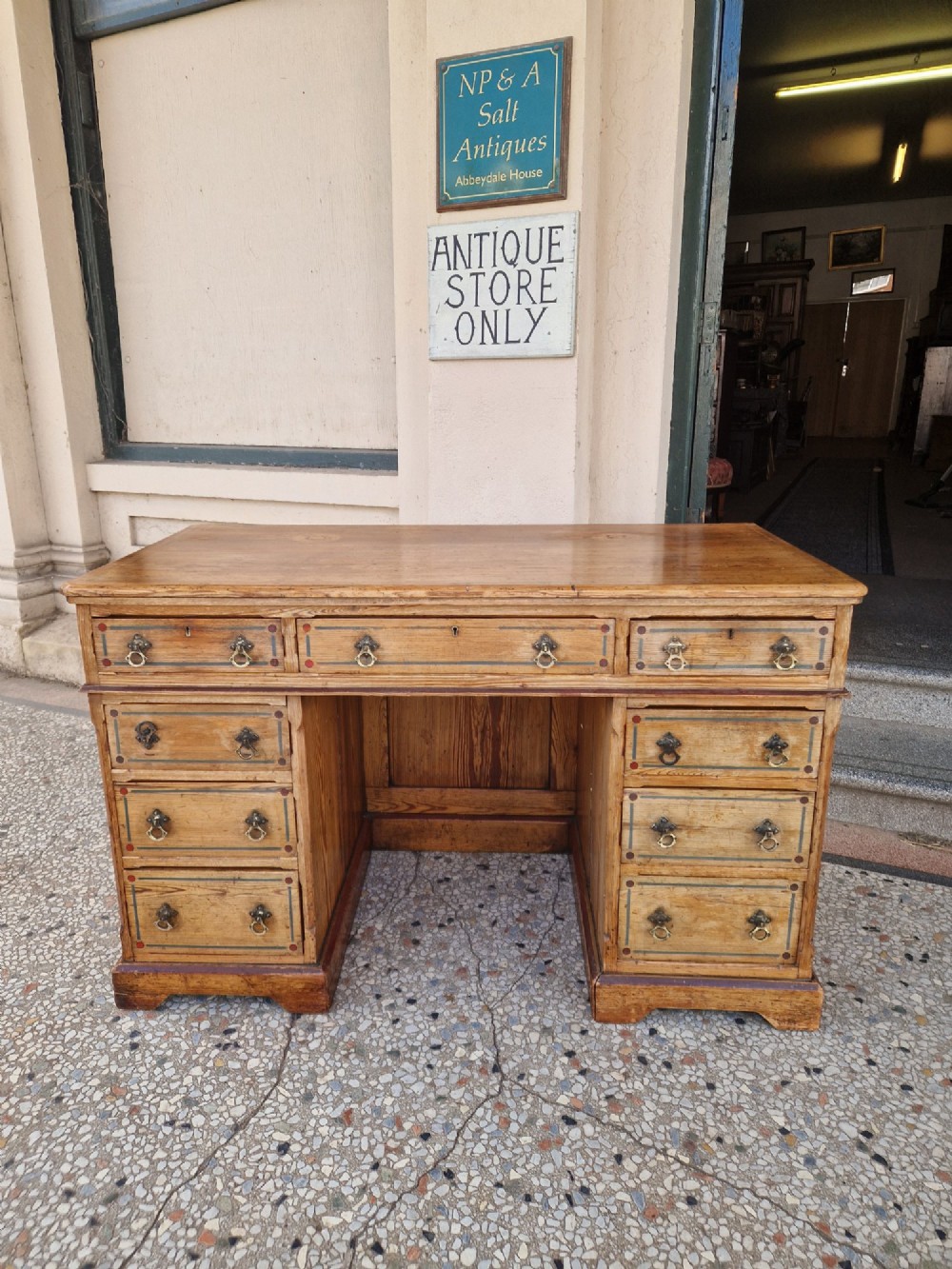 An Arts and Crafts pitch pine pedestal desk featuring nine drawers with hand-painted line borders and metal ring handles.