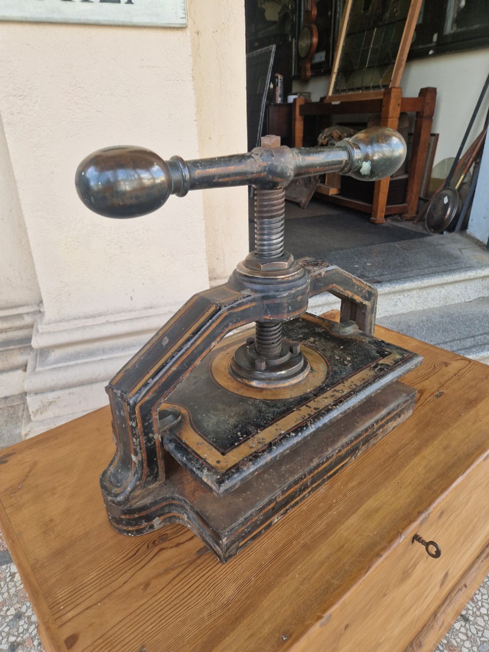 A heavy black cast iron book press featuring a central screw mechanism with oversized rounded handles and painted gold line detailing. View II