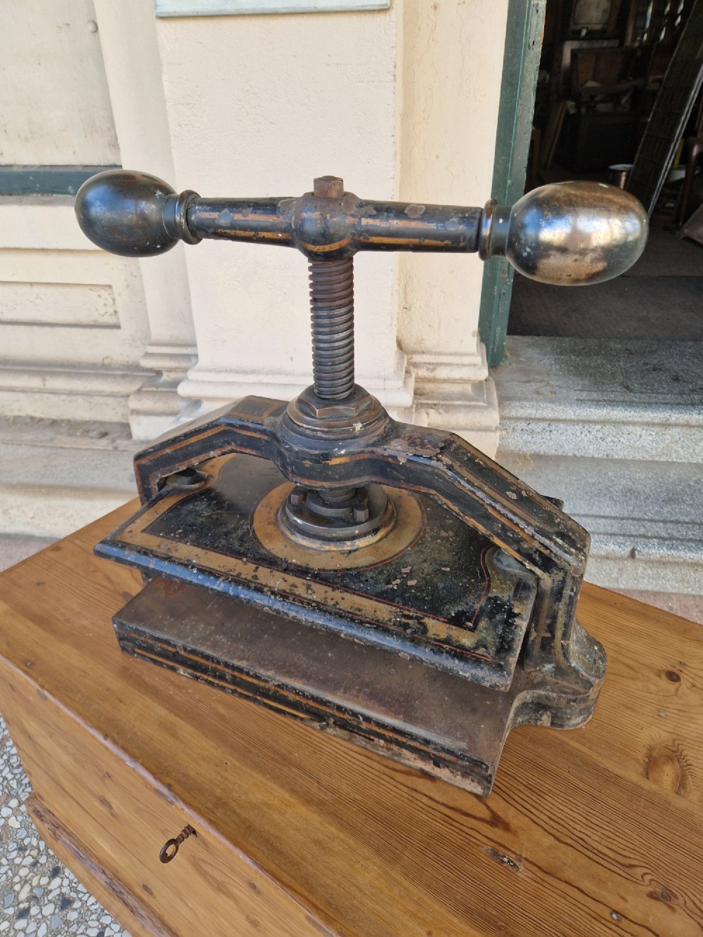A heavy black cast iron book press featuring a central screw mechanism with oversized rounded handles and painted gold line detailing. View IV