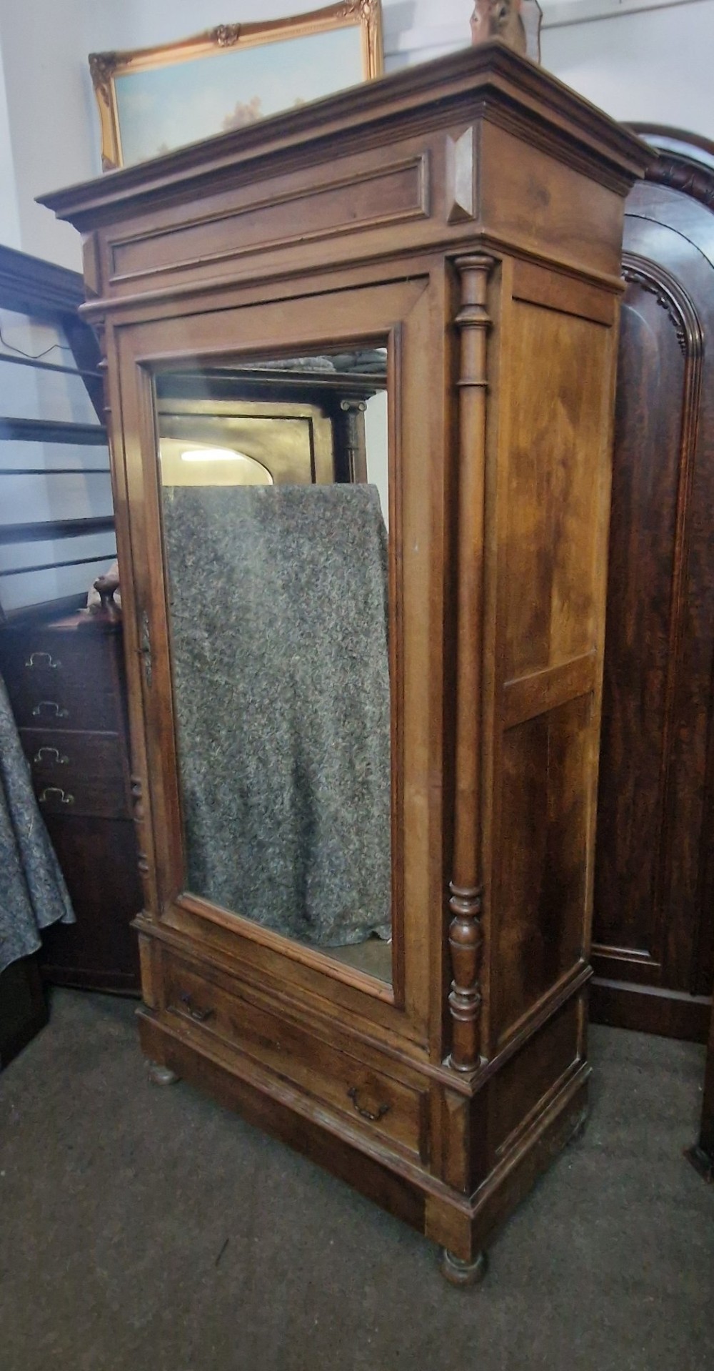 An antique burr walnut single-door armoire with a central bevelled mirror, flanking turned columns, and a lower drawer. View XIII