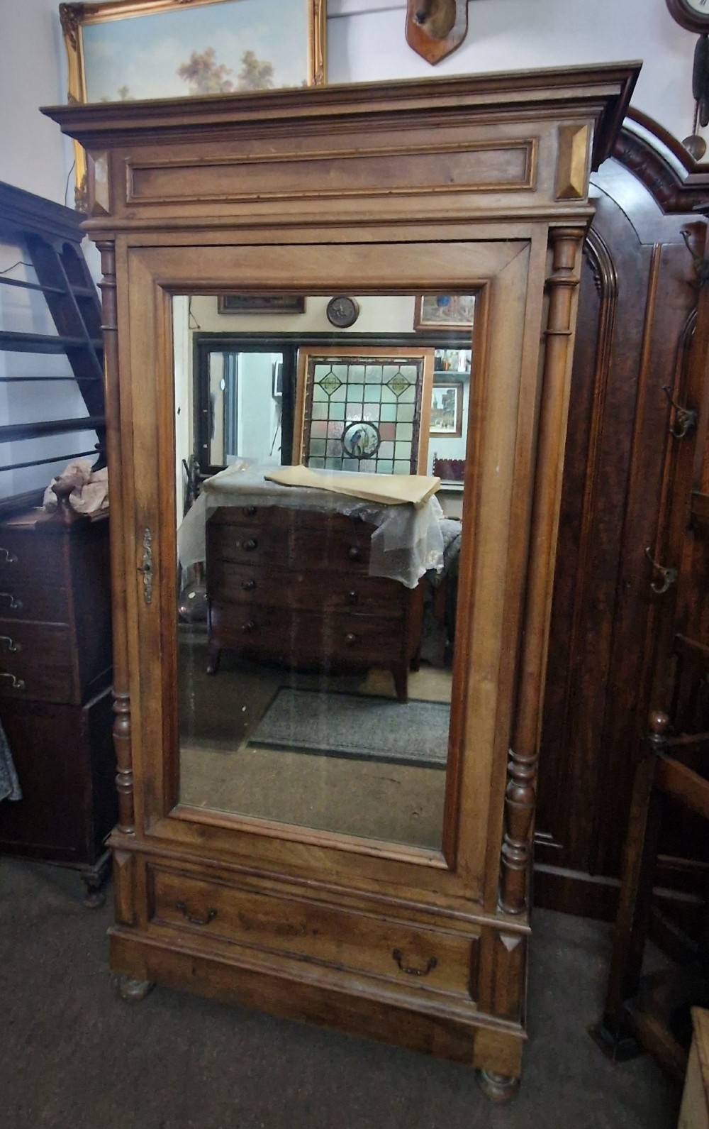 An antique burr walnut single-door armoire with a central bevelled mirror, flanking turned columns, and a lower drawer.