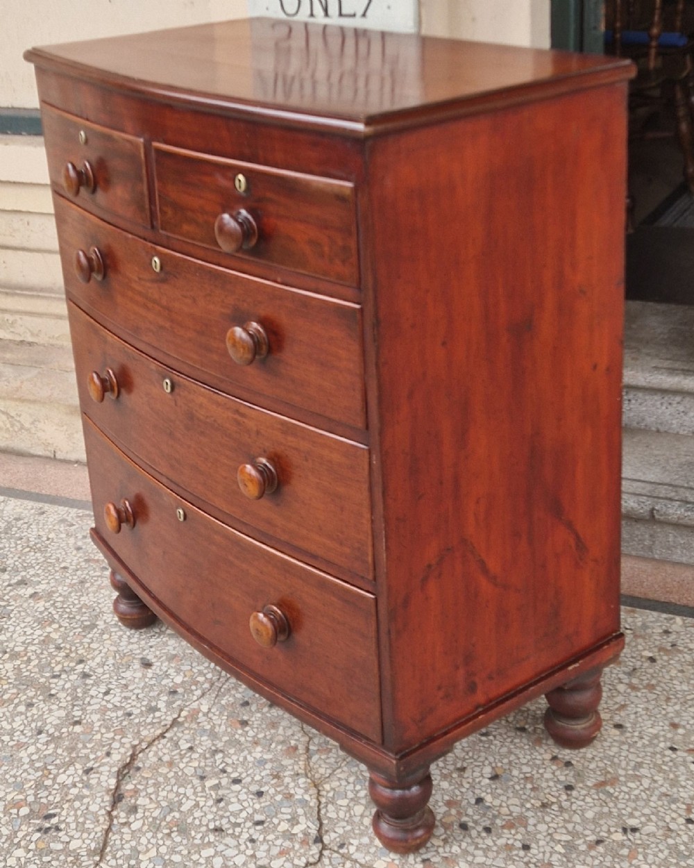 A Victorian mahogany bow fronted chest of drawers featuring two short over three long drawers with turned wooden handles and brass escutcheons on turned feet. View III